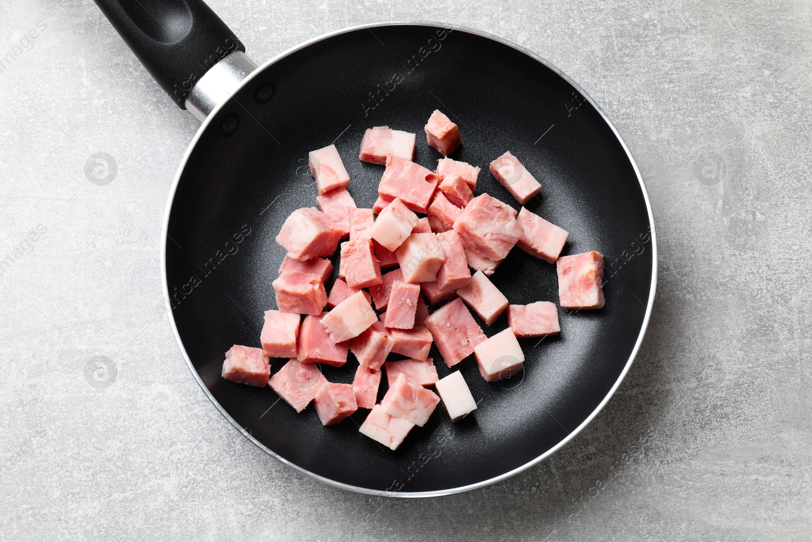 Photo of Pieces of fresh bacon in frying pan on grey textured table, top view