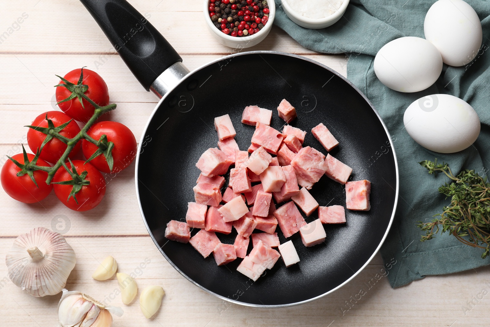 Photo of Pieces of fresh bacon in frying pan and products on light wooden table, flat lay