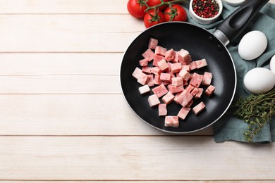 Photo of Pieces of fresh bacon in frying pan and products on light wooden table, flat lay. Space for text