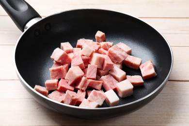 Photo of Pieces of fresh bacon in frying pan on light wooden table, closeup