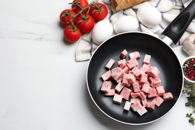 Photo of Pieces of fresh bacon in frying pan and products on white marble table, flat lay. Space for text