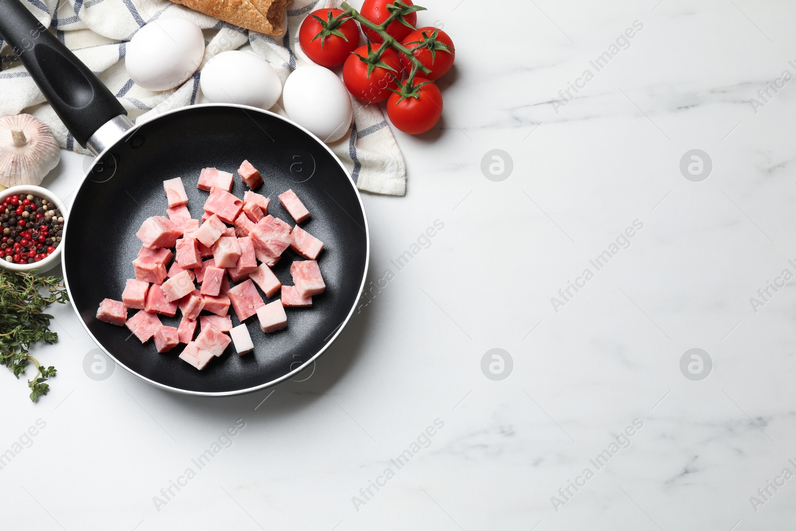 Photo of Pieces of fresh bacon in frying pan and products on white marble table, flat lay. Space for text