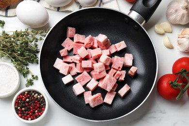 Photo of Pieces of fresh bacon in frying pan and products on white table, flat lay