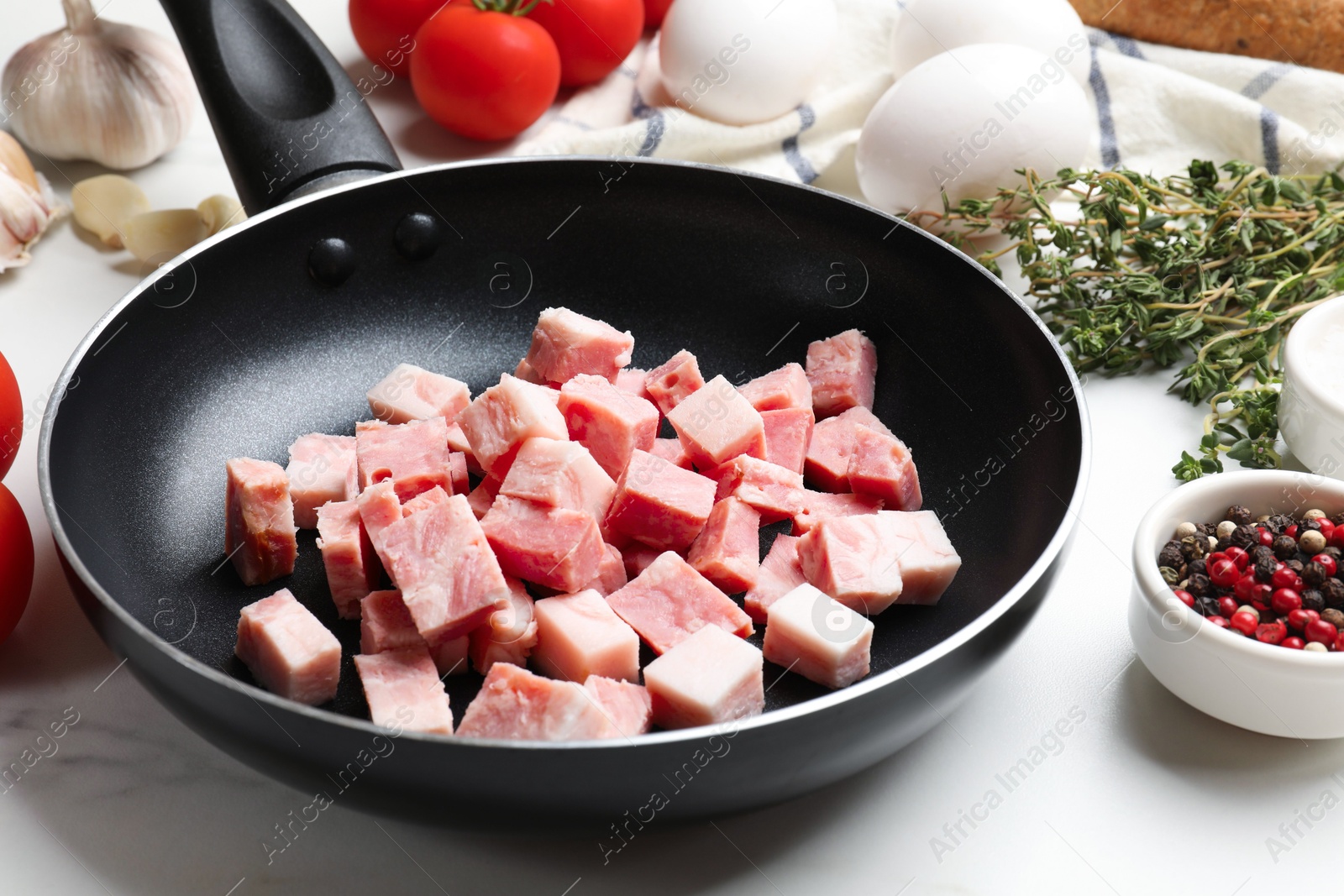 Photo of Pieces of fresh bacon in frying pan and peppercorns on white table, closeup