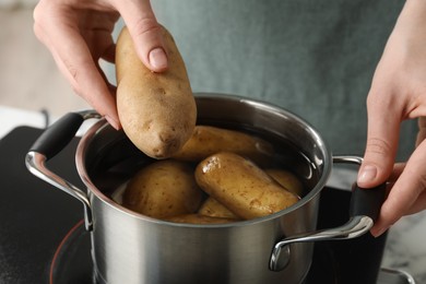 Photo of Woman putting potato into metal pot on stove, closeup