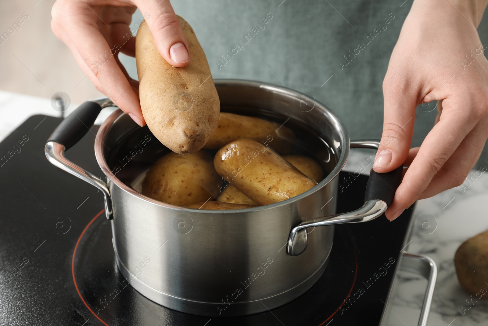 Photo of Woman putting potato into metal pot on stove, closeup