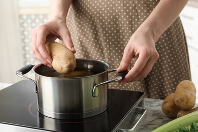 Woman putting potato into metal pot on stove, closeup