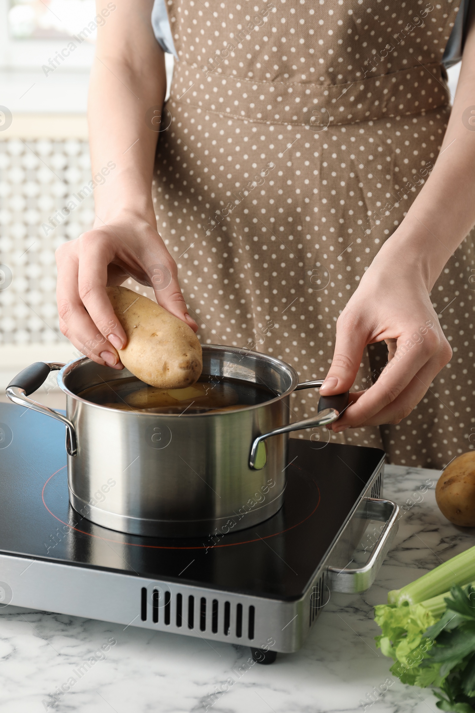 Photo of Woman putting potato into metal pot on stove, closeup