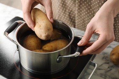 Woman putting potato into metal pot on stove, closeup