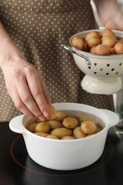 Woman putting potato into metal pot on stove, closeup