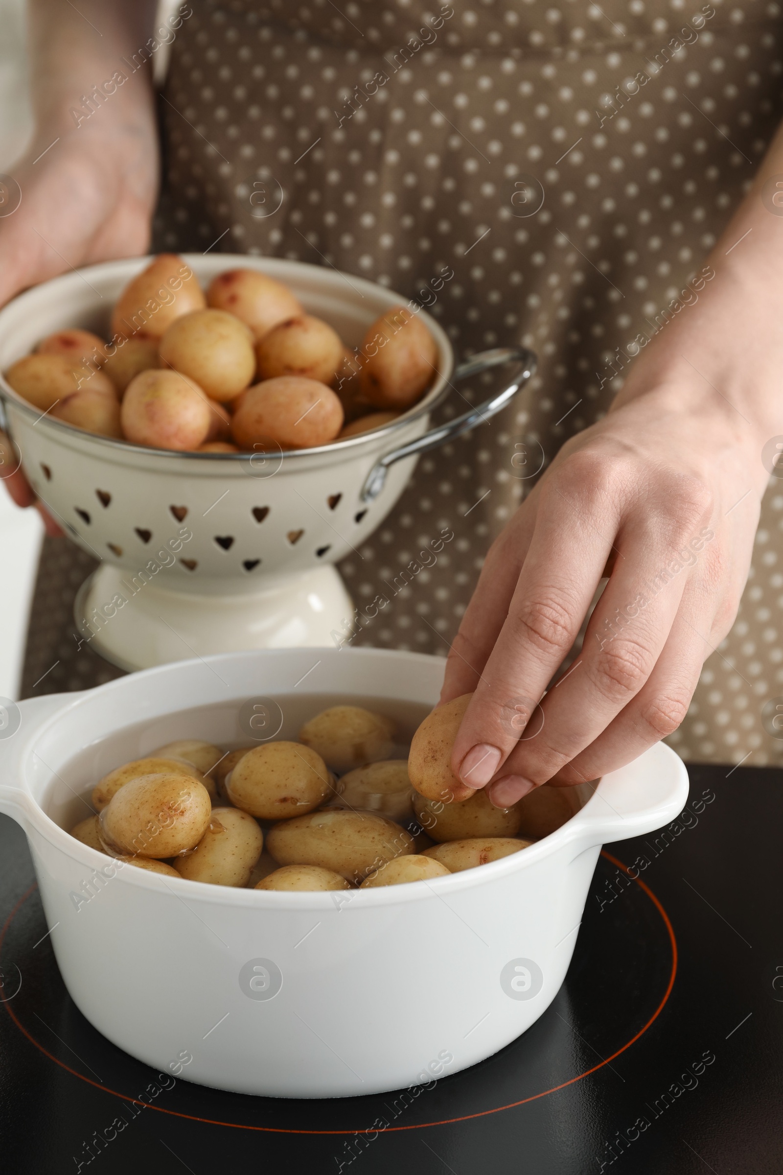 Photo of Woman putting potato into metal pot on stove, closeup