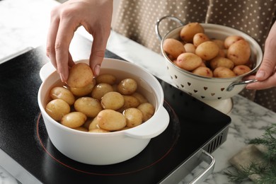 Photo of Woman putting potato into metal pot on stove, closeup