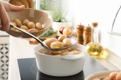 Photo of Woman taking potatoes from pot on stove, closeup