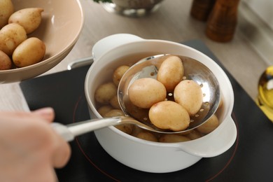 Woman taking potatoes from pot on stove, closeup