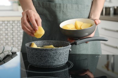 Photo of Woman putting potato into saucepan on stove, closeup