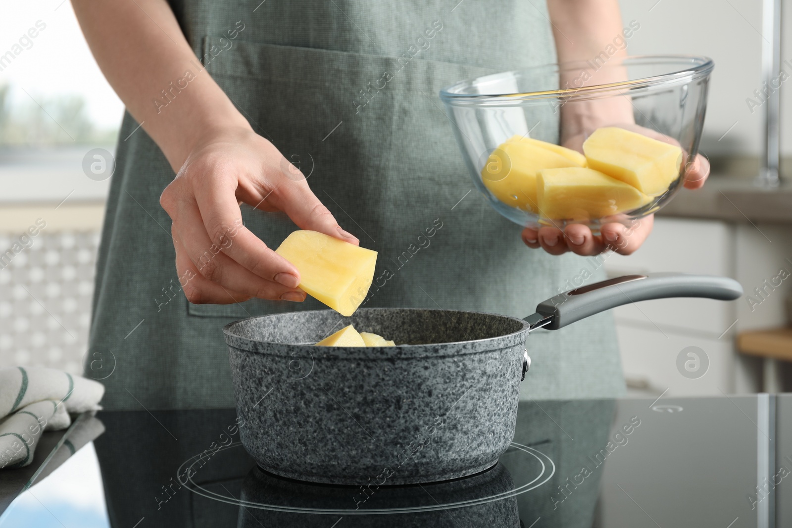 Photo of Woman putting potato into saucepan on stove, closeup