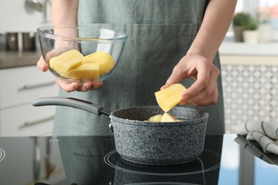 Photo of Woman putting potato into saucepan on stove, closeup