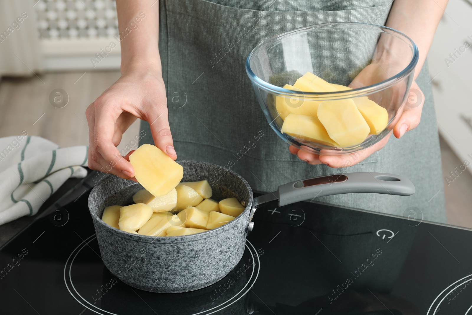 Photo of Woman putting potato into saucepan on stove, closeup