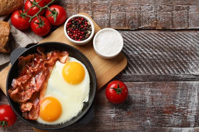 Tasty bacon with eggs in dish and products on wooden table, flat lay. Space for text