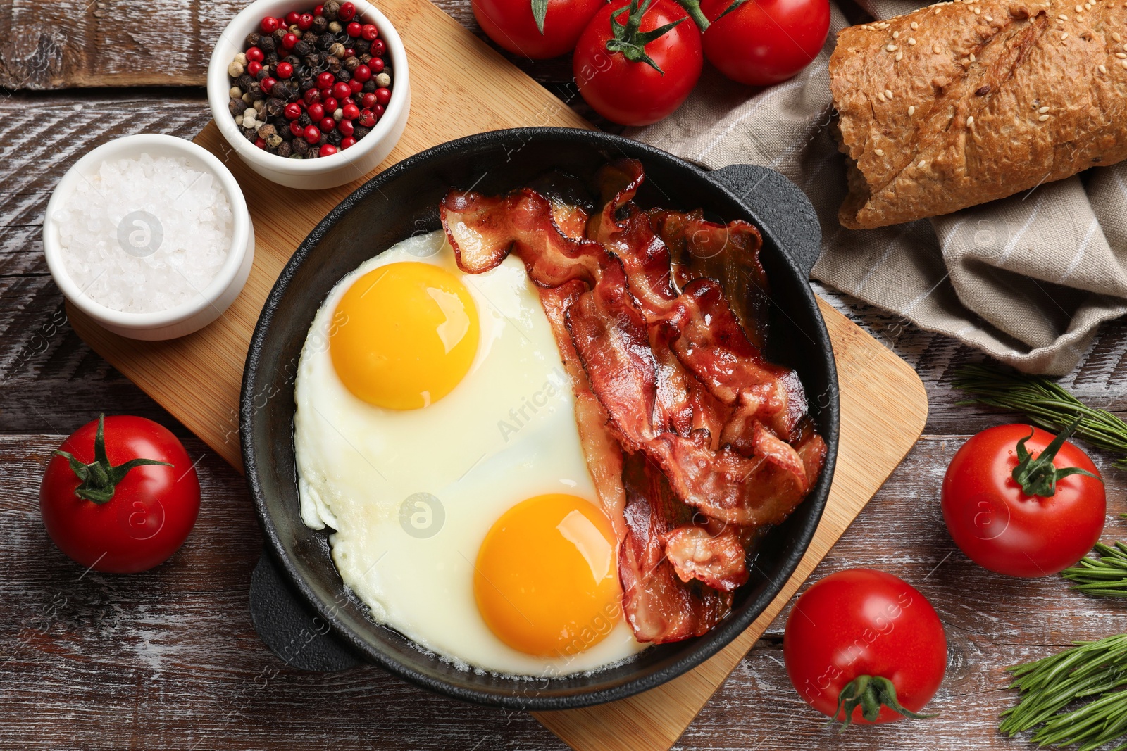 Photo of Tasty bacon and eggs in dish among products on wooden table, flat lay