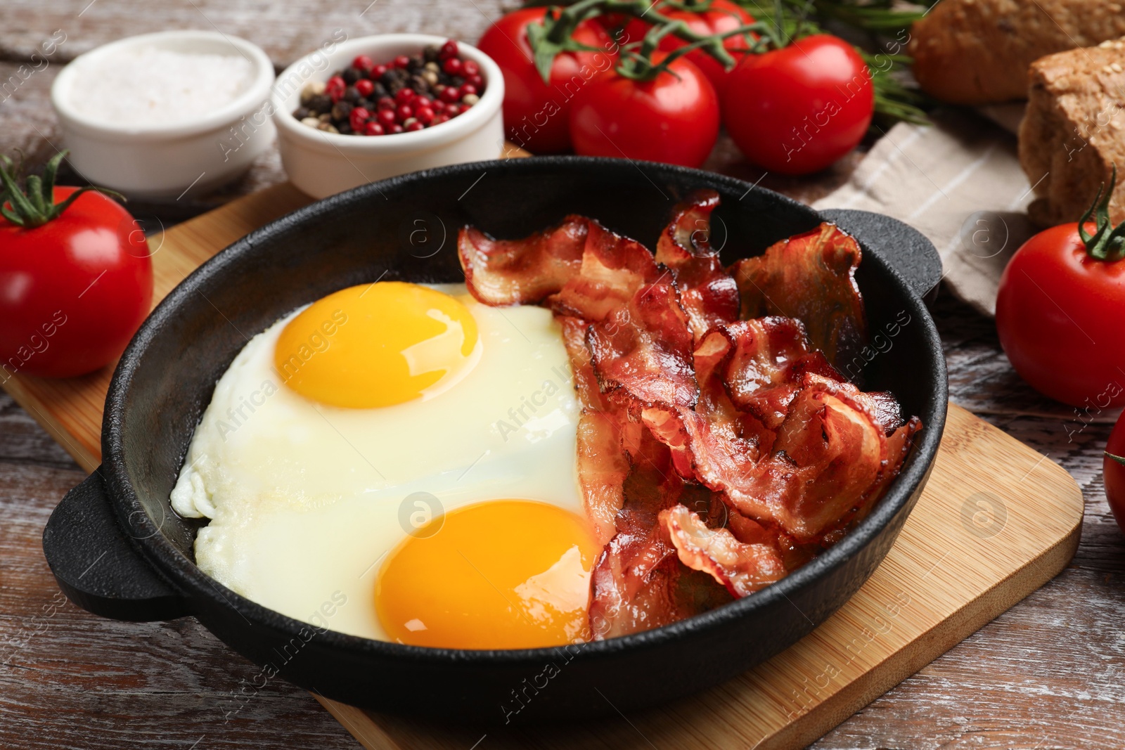 Photo of Tasty bacon with eggs in dish and products on wooden table, closeup