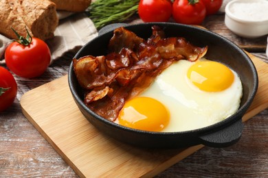 Tasty bacon with eggs in dish and products on wooden table, closeup