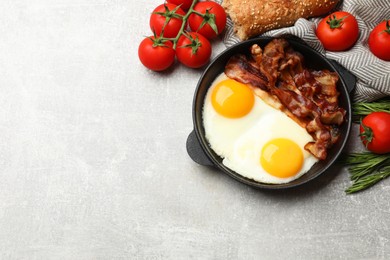 Tasty bacon with eggs in dish and products on gray textured table, flat lay. Space for text