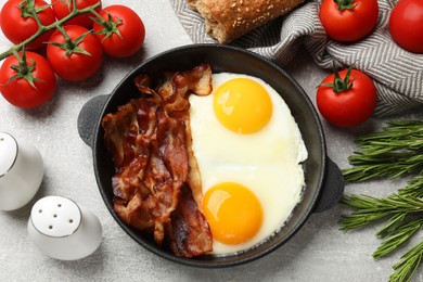 Photo of Tasty bacon and eggs in dish among products on gray textured table, flat lay