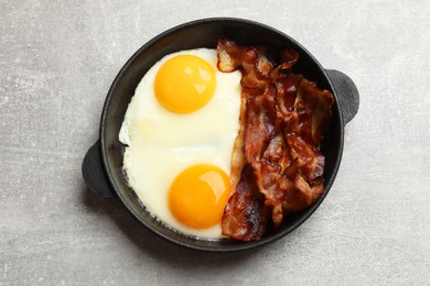 Photo of Tasty bacon and eggs in dish on gray textured table, top view