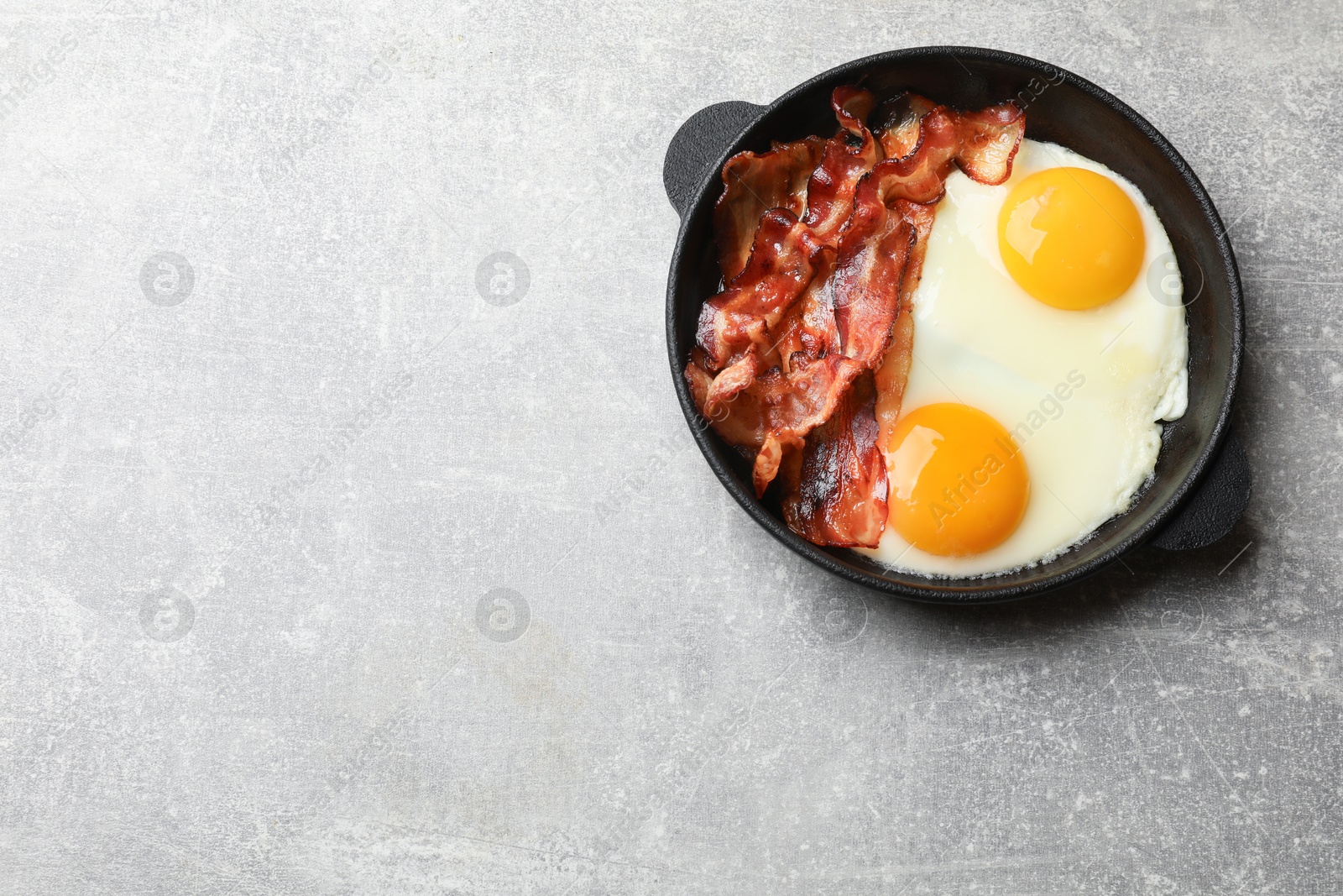 Photo of Tasty bacon and eggs in dish on gray textured table, top view. Space for text