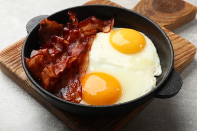 Tasty bacon and eggs in dish on gray textured table, closeup