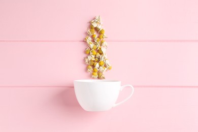 Photo of Chamomile flowers and white cup on pink wooden table, top view
