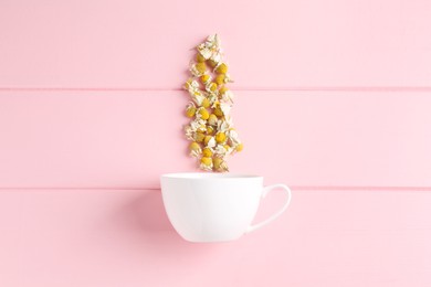 Chamomile flowers and white cup on pink wooden table, top view