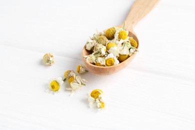 Photo of Chamomile flowers in spoon on white wooden table