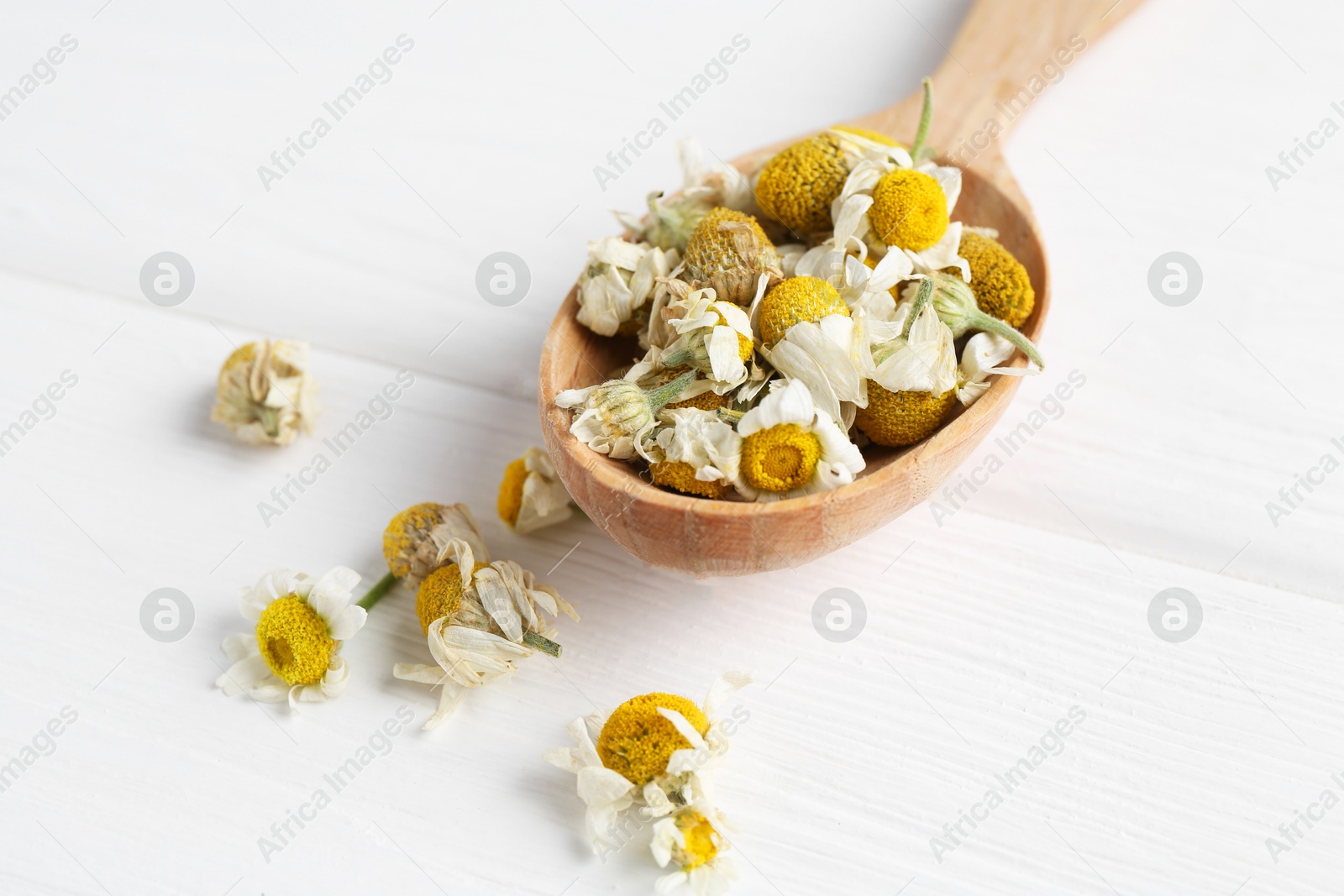 Photo of Chamomile flowers in spoon on white wooden table