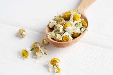 Chamomile flowers in spoon on white wooden table