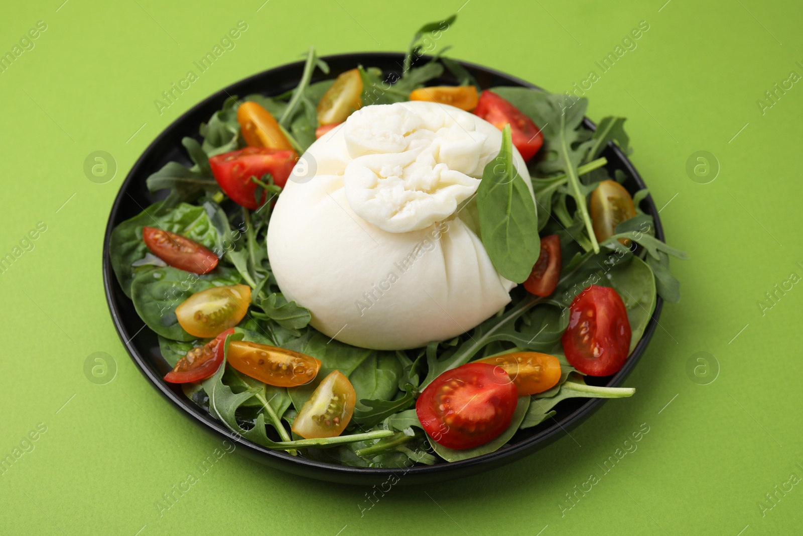 Photo of Delicious burrata salad on green table, closeup