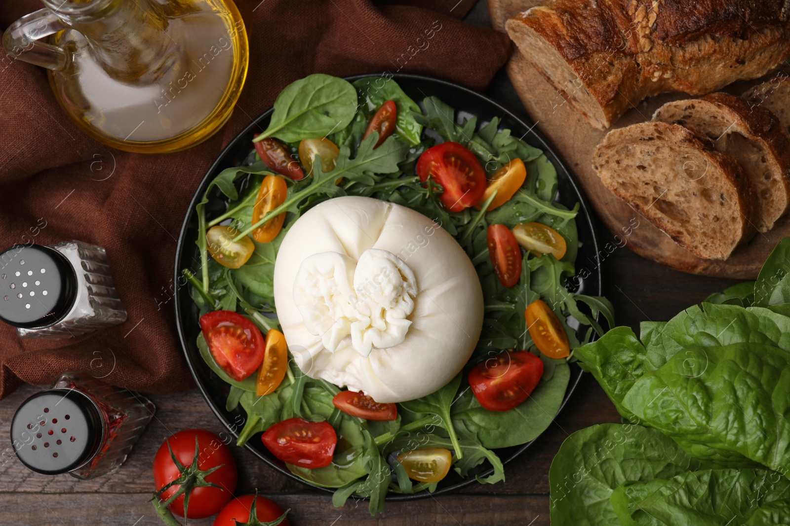 Photo of Delicious burrata salad and products on wooden table, flat lay