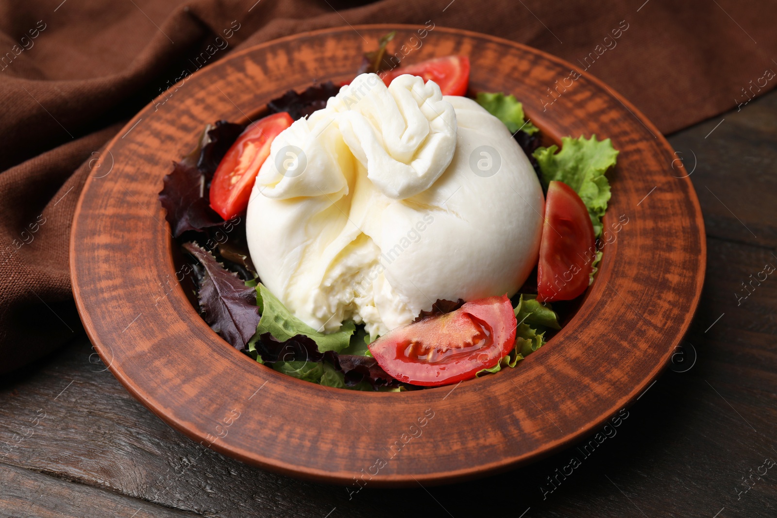 Photo of Delicious burrata salad in bowl on wooden table, closeup