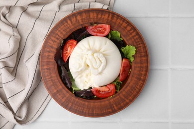 Photo of Delicious burrata salad in bowl on white tiled table, top view