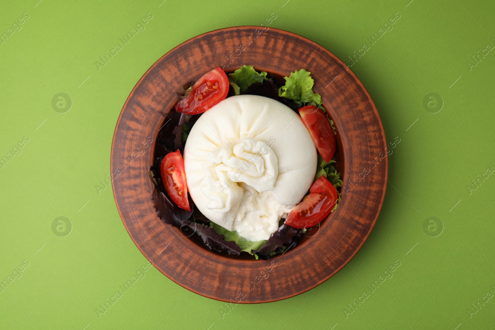 Photo of Delicious burrata salad in bowl on green table, top view