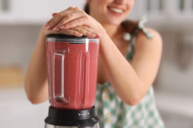 Woman making delicious smoothie with blender in kitchen, closeup