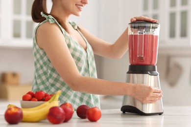 Woman making delicious smoothie with blender at white marble table in kitchen, closeup