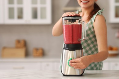 Photo of Woman making delicious smoothie with blender at white marble table in kitchen, closeup. Space for text