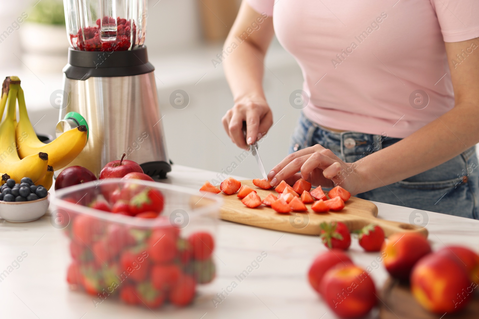 Photo of Woman making delicious smoothie with blender at white marble table in kitchen, closeup