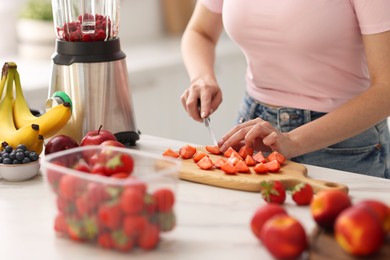 Woman making delicious smoothie with blender at white marble table in kitchen, closeup