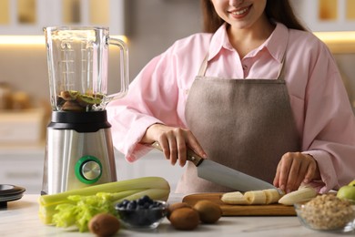 Photo of Woman making delicious smoothie with blender at white marble table in kitchen, closeup