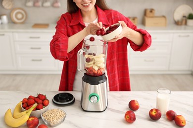 Woman making delicious smoothie with blender at white marble table in kitchen, closeup