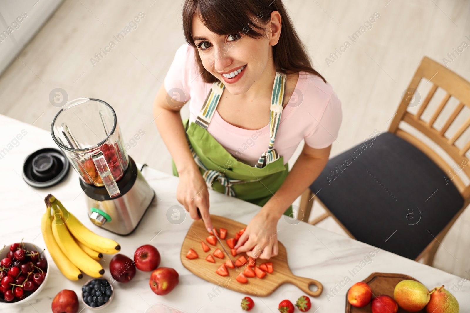 Photo of Young woman making delicious smoothie with blender at white marble table in kitchen, above view