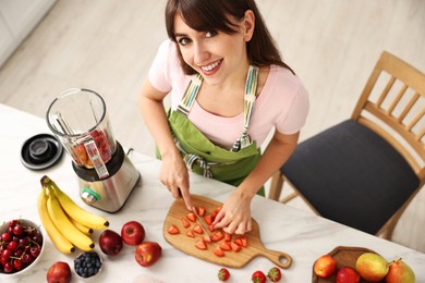 Young woman making delicious smoothie with blender at white marble table in kitchen, above view